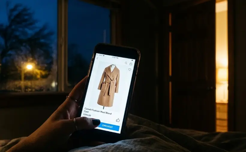The Midnight Almost-Purchase smartphone screen displaying long camel coat thumb hovering over checkout button late night impulse