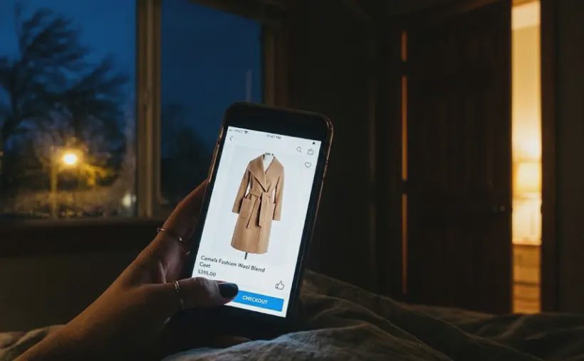 smartphone screen displaying long camel coat thumb hovering over checkout button late night impulse