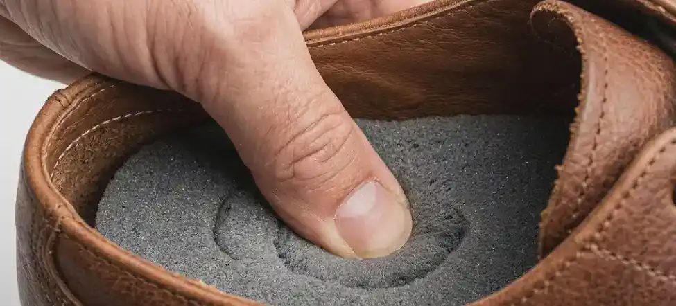 thumb pressing into leather shoe insole cushion test yielding foam white daylight